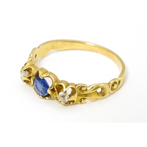 650 - A yellow metal ring set with central sapphire flanked by diamonds. Ring size approx. J