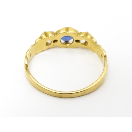 650 - A yellow metal ring set with central sapphire flanked by diamonds. Ring size approx. J