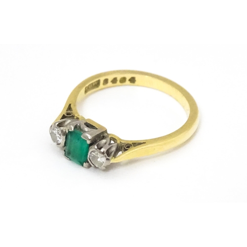 659 - An 18ct gold ring set with central emerald flanked by diamonds. Ring size approx K 1/2