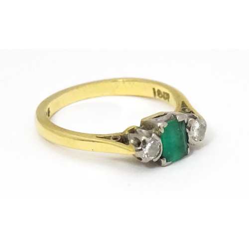 659 - An 18ct gold ring set with central emerald flanked by diamonds. Ring size approx K 1/2