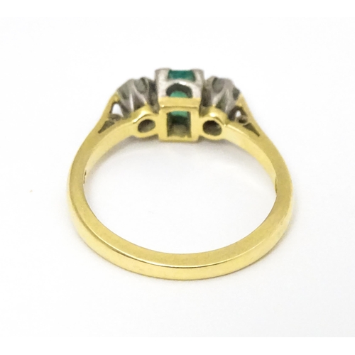 659 - An 18ct gold ring set with central emerald flanked by diamonds. Ring size approx K 1/2