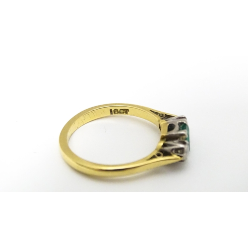 659 - An 18ct gold ring set with central emerald flanked by diamonds. Ring size approx K 1/2