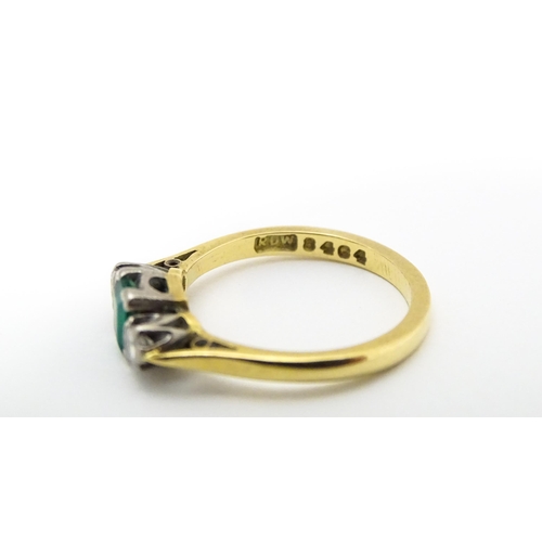 659 - An 18ct gold ring set with central emerald flanked by diamonds. Ring size approx K 1/2