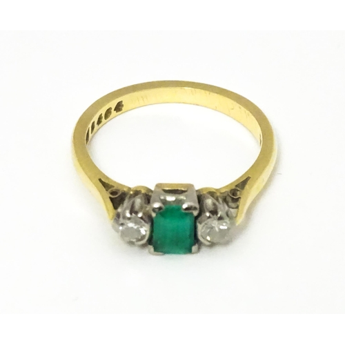 659 - An 18ct gold ring set with central emerald flanked by diamonds. Ring size approx K 1/2