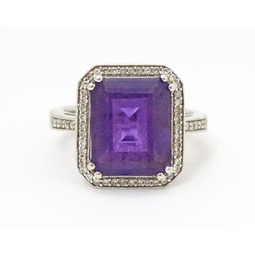 679 - An 18ct gold ring set with central amethyst bordered by diamonds with further diamonds to shoulders.... 