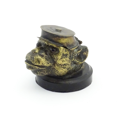 1192 - A Victorian novelty brass desk inkwell formed as the head of a monkey with glass eyes wearing a hat.... 