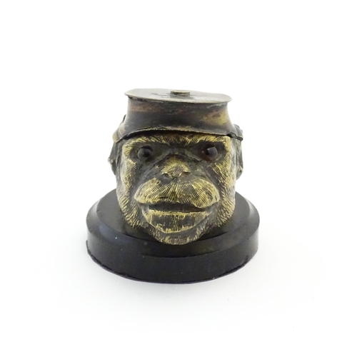 1192 - A Victorian novelty brass desk inkwell formed as the head of a monkey with glass eyes wearing a hat.... 