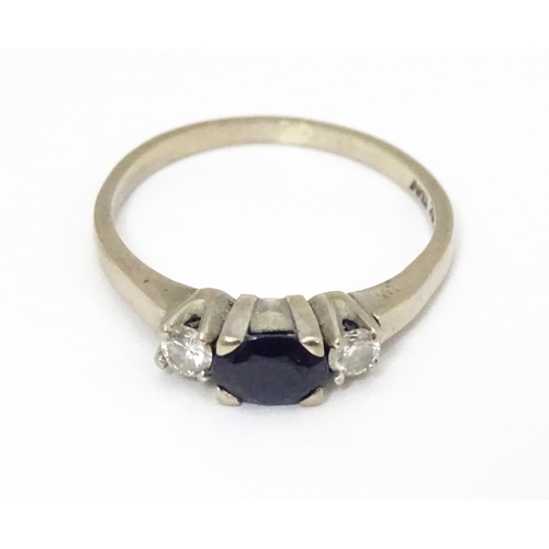 645 - An 18ct white gold ring set with central sapphire flanked by diamonds. Ring size approx. M 1/2