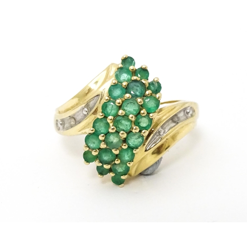 613 - An 18ct gold ring set with emeralds, flanked by a diamond to each shoulder. Ring size approx L.