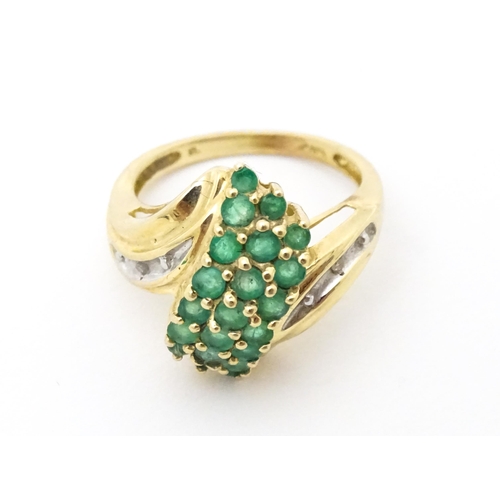 613 - An 18ct gold ring set with emeralds, flanked by a diamond to each shoulder. Ring size approx L.