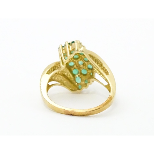 613 - An 18ct gold ring set with emeralds, flanked by a diamond to each shoulder. Ring size approx L.