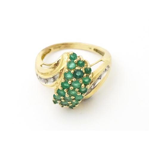 613 - An 18ct gold ring set with emeralds, flanked by a diamond to each shoulder. Ring size approx L.