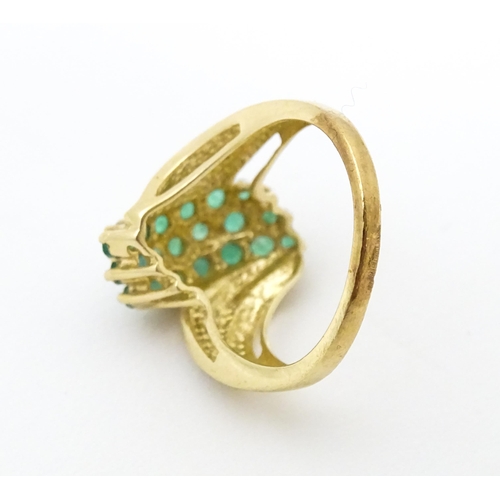 613 - An 18ct gold ring set with emeralds, flanked by a diamond to each shoulder. Ring size approx L.