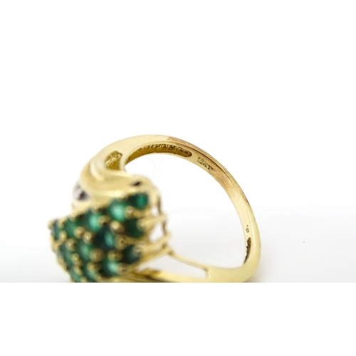 613 - An 18ct gold ring set with emeralds, flanked by a diamond to each shoulder. Ring size approx L.