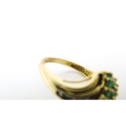 613 - An 18ct gold ring set with emeralds, flanked by a diamond to each shoulder. Ring size approx L.