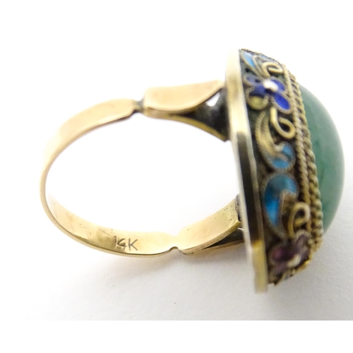 638 - A 14ct gold ring set with central jadeite cabochon  bordered by floral enamel detail. Ring size appr... 