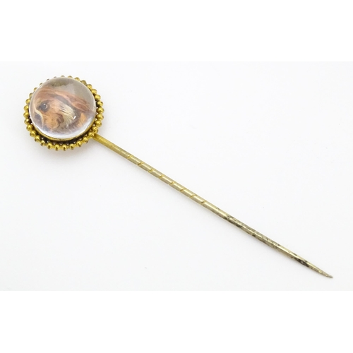 666 - A gilt metal stick pin surmounted by an Essex Crystal cabochon with dog head decoration. Cabochon ap... 