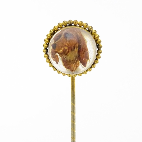 666 - A gilt metal stick pin surmounted by an Essex Crystal cabochon with dog head decoration. Cabochon ap... 