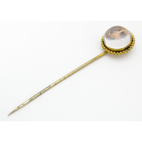 666 - A gilt metal stick pin surmounted by an Essex Crystal cabochon with dog head decoration. Cabochon ap... 