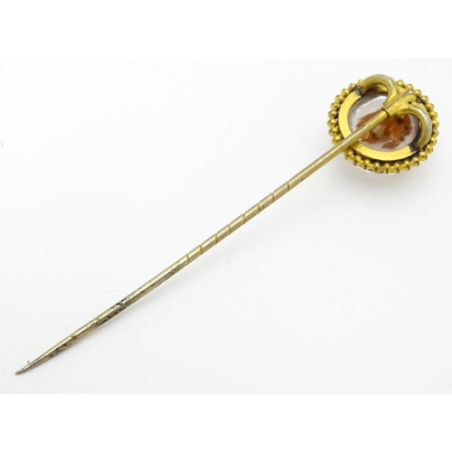 666 - A gilt metal stick pin surmounted by an Essex Crystal cabochon with dog head decoration. Cabochon ap... 