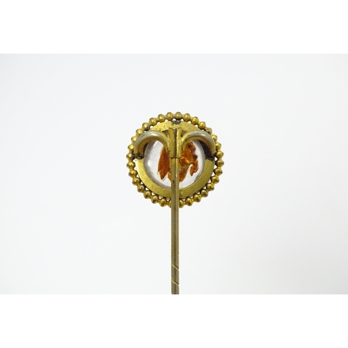 666 - A gilt metal stick pin surmounted by an Essex Crystal cabochon with dog head decoration. Cabochon ap... 