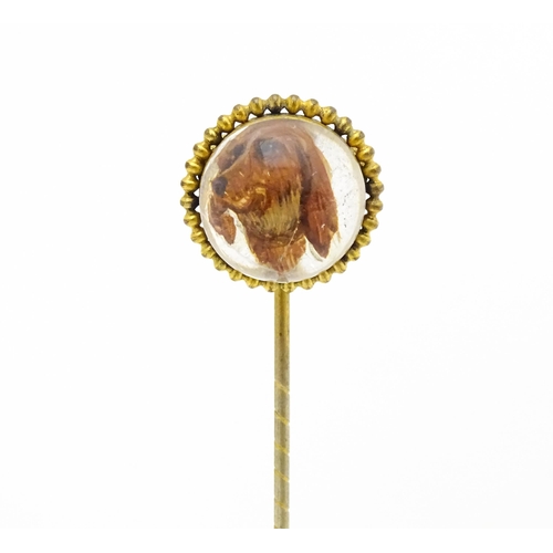 666 - A gilt metal stick pin surmounted by an Essex Crystal cabochon with dog head decoration. Cabochon ap... 