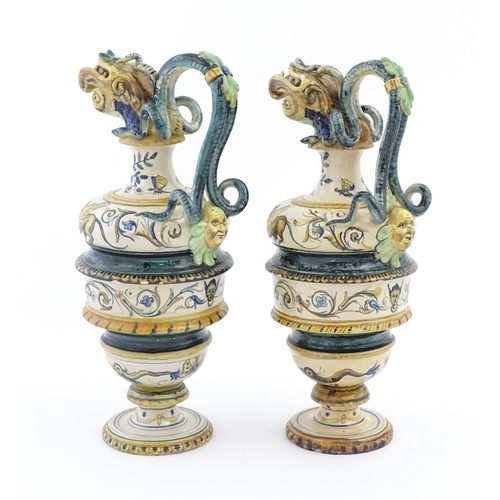 174 - A pair of Italian maiolica wine ewers with fish head spouts, scrolling handles and relief mask detai... 