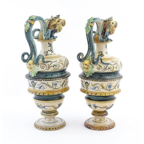 174 - A pair of Italian maiolica wine ewers with fish head spouts, scrolling handles and relief mask detai... 