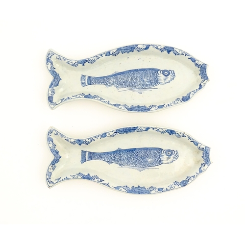 Two Dutch Delft blue and white herring dishes of stylised fish form, with hand painted decoration depicting a herring to centre with floral and foliate border. Approx. 10 1/4" wide (2)