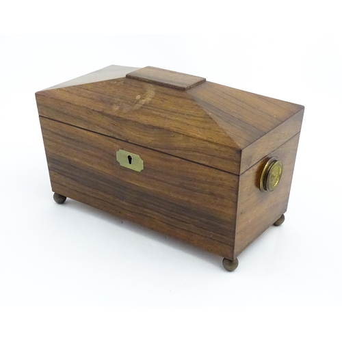 1062 - A 19thC rosewood tea caddy of sarcophagus form with twin roundel handles and ball feet. The interior... 