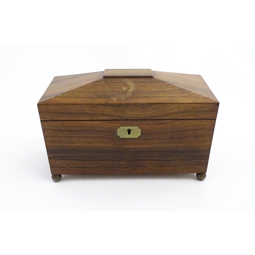 1062 - A 19thC rosewood tea caddy of sarcophagus form with twin roundel handles and ball feet. The interior... 