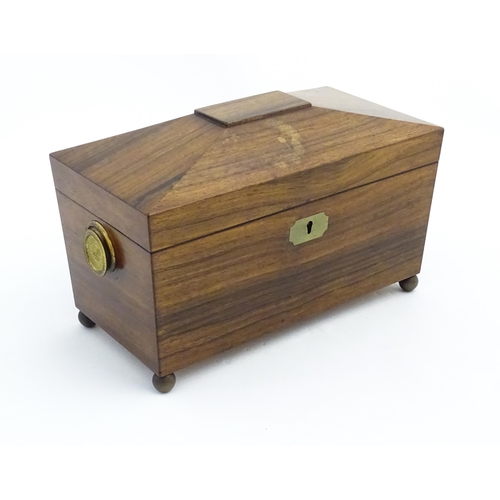 1062 - A 19thC rosewood tea caddy of sarcophagus form with twin roundel handles and ball feet. The interior... 