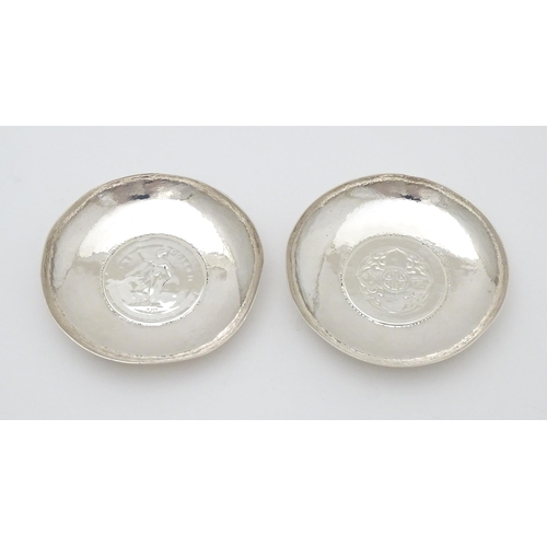 341 - A pair of white metal pin dishes with hammered decoration and inset coin medallions to base. Possibl... 