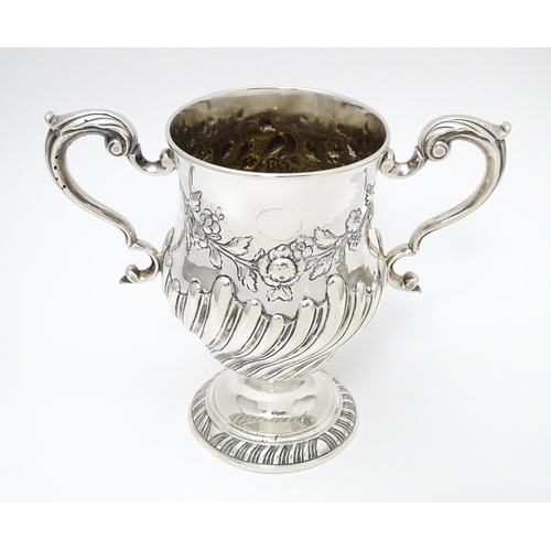 409 - A 19thC Irish silver twin handled pedestal cup with fluted body, and embossed floral and foliate swa... 