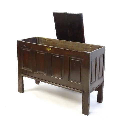 1337 - An early 18thC oak coffer with a removeable lid above a panelled front and sides raised on four tall... 