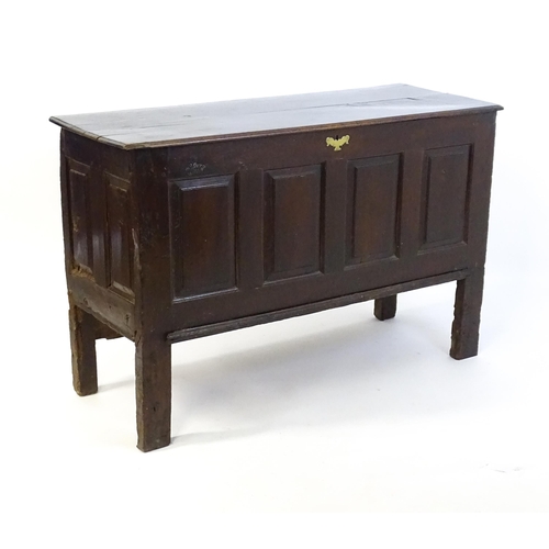 1337 - An early 18thC oak coffer with a removeable lid above a panelled front and sides raised on four tall... 