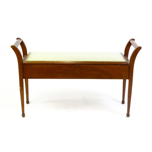 1459 - An early 20thC mahogany piano stool flanked by carrying handles with an upholstered, hinged seat abo... 