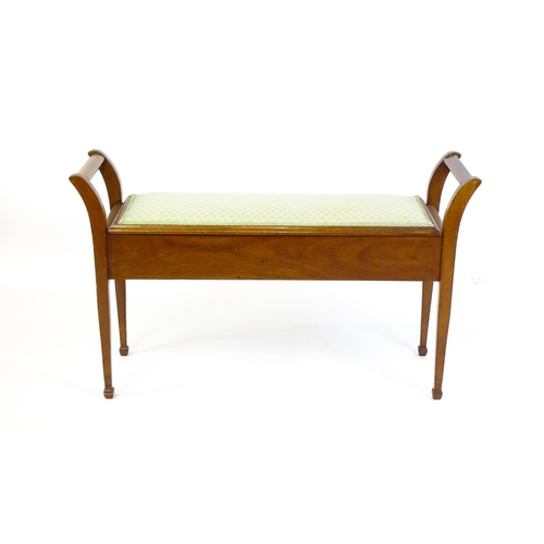 1459 - An early 20thC mahogany piano stool flanked by carrying handles with an upholstered, hinged seat abo... 