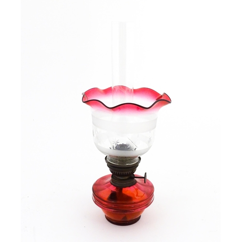 1314 - An early 20thC table oil lamp, the cranberry glass reservoir supporting a brass burner (marked 'Popu... 