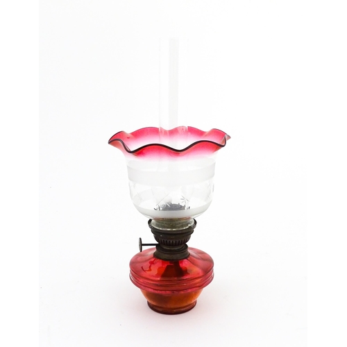 1314 - An early 20thC table oil lamp, the cranberry glass reservoir supporting a brass burner (marked 'Popu... 