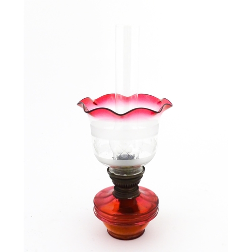 1314 - An early 20thC table oil lamp, the cranberry glass reservoir supporting a brass burner (marked 'Popu... 