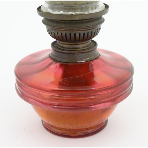 1314 - An early 20thC table oil lamp, the cranberry glass reservoir supporting a brass burner (marked 'Popu... 