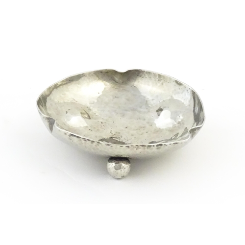 1003 - An Arts and Crafts white metal bonbon dish of shaped form with hammered decoration and three ball fe... 