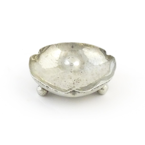 1003 - An Arts and Crafts white metal bonbon dish of shaped form with hammered decoration and three ball fe... 