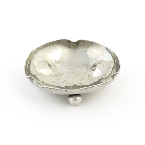 1003 - An Arts and Crafts white metal bonbon dish of shaped form with hammered decoration and three ball fe... 