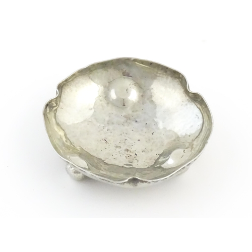 1003 - An Arts and Crafts white metal bonbon dish of shaped form with hammered decoration and three ball fe... 