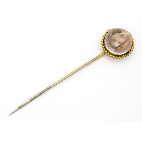 666 - A gilt metal stick pin surmounted by an Essex Crystal cabochon with dog head decoration. Cabochon ap... 