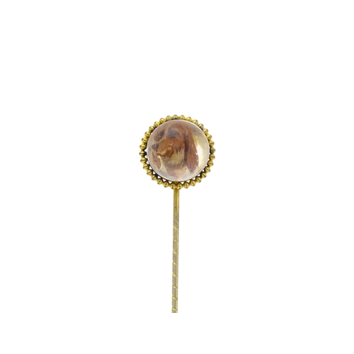 666 - A gilt metal stick pin surmounted by an Essex Crystal cabochon with dog head decoration. Cabochon ap... 