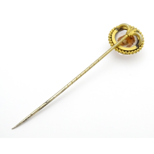 666 - A gilt metal stick pin surmounted by an Essex Crystal cabochon with dog head decoration. Cabochon ap... 