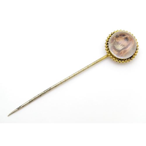 666 - A gilt metal stick pin surmounted by an Essex Crystal cabochon with dog head decoration. Cabochon ap... 